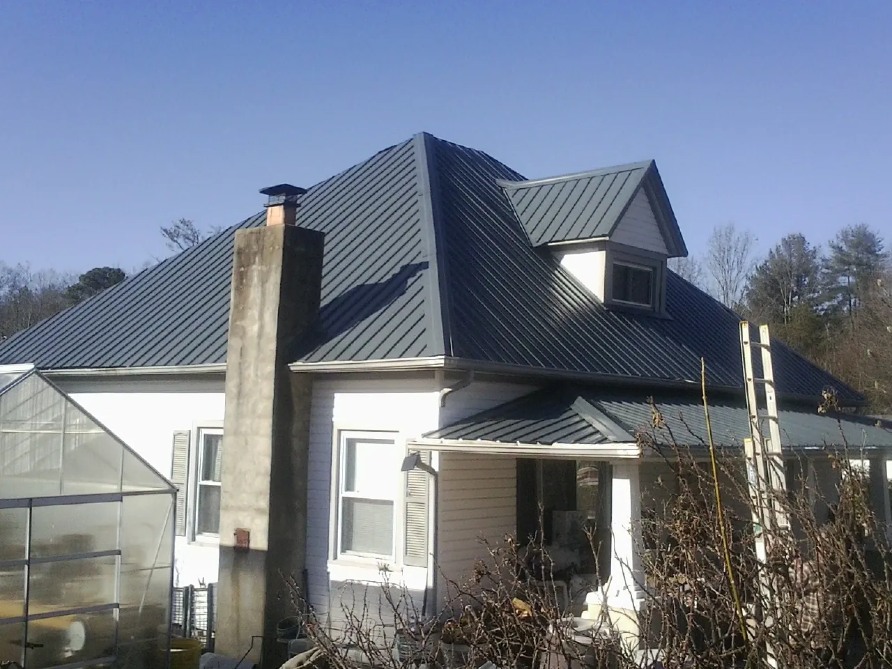 Dark blue standing seam metal roof on a white farmhouse with dormer — Slate & Tile Roof Repair by Roofing Brothers in Plush