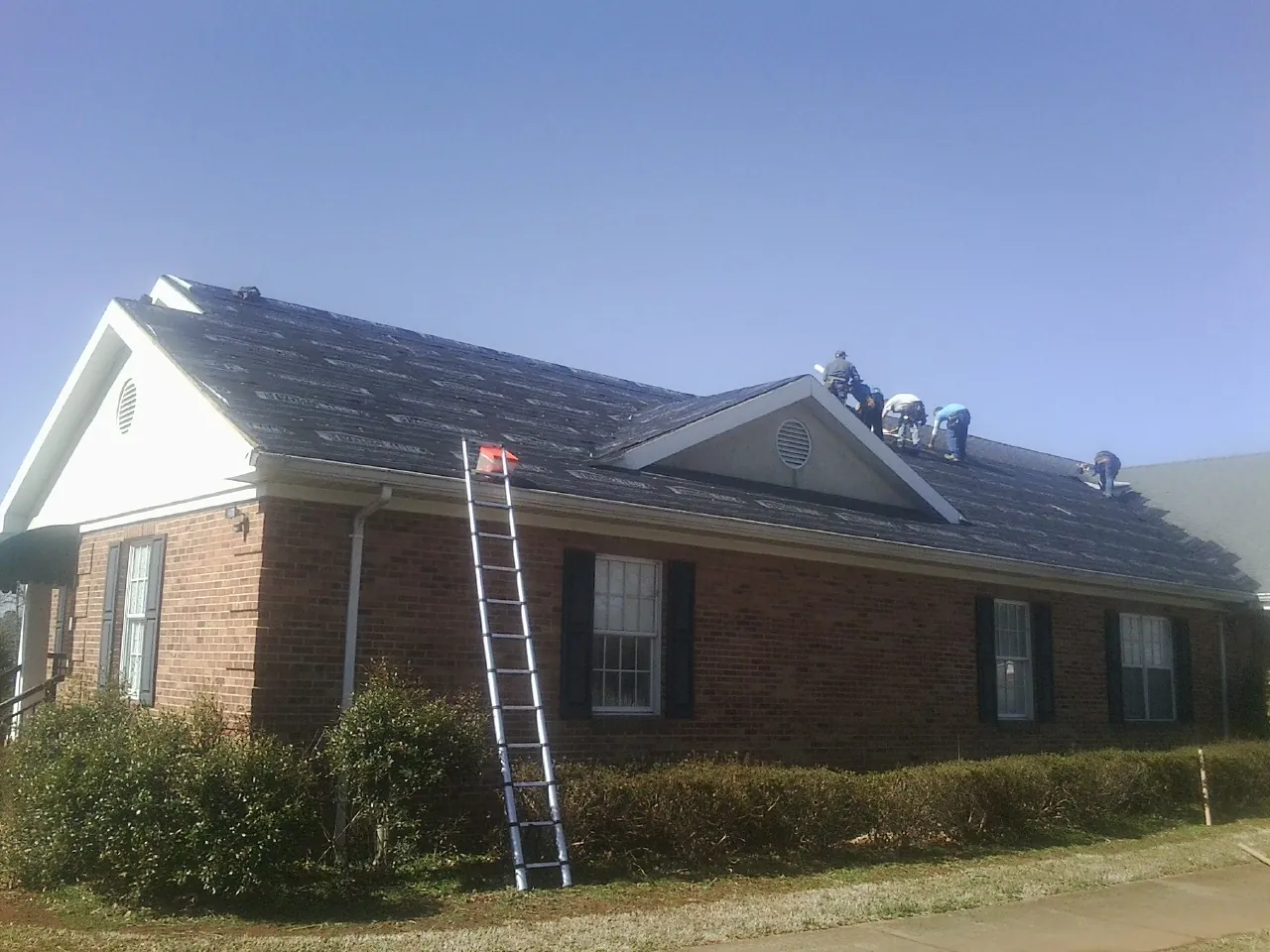 Crew tearing shingles off a brick ranch roof with a ladder set — Metal Roof Repair work by our crew in Plush