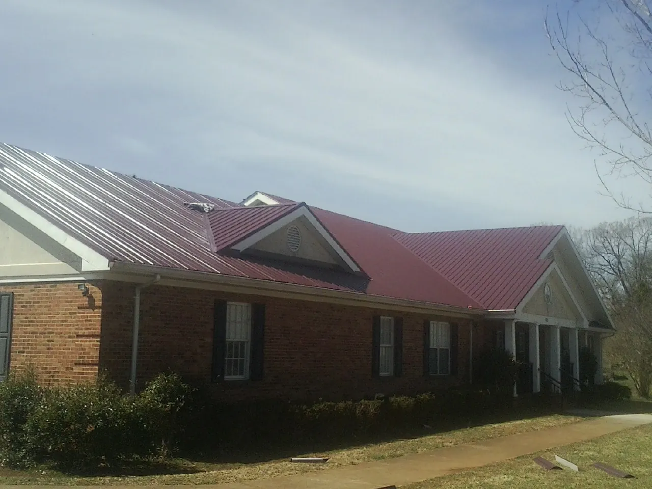 Red metal roof with gabled entries on a long brick building, from a Hail Damage Roof Repair job in Plush
