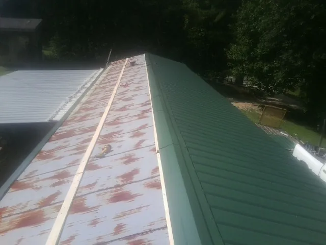 Old rusted panels beside newly installed green metal roofing — Wind Damage Roof Repair by Roofing Brothers in Plush