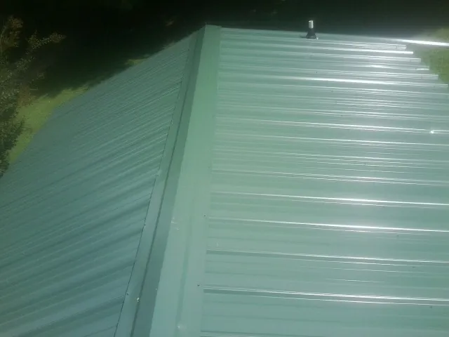 New green metal panels meeting at the ridge of a roof — Flat Roof Repair work by our crew in Plush