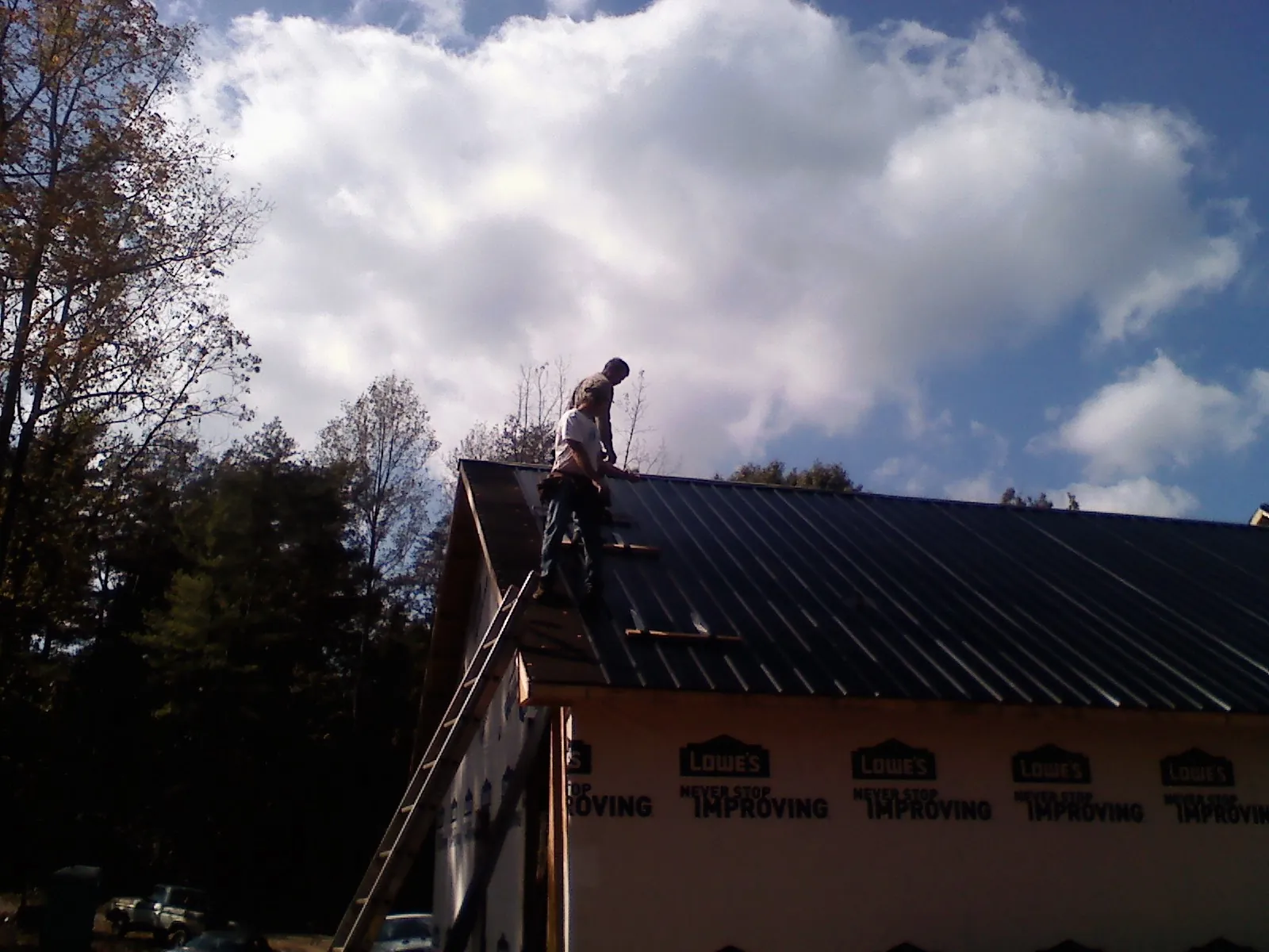 Roofer fastening dark metal panels high against a cloudy sky, from a Roof Inspection job in Plush